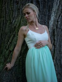 Woman in dress standing against tree trunk