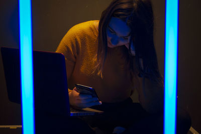 Woman using mobile phone and laptop while sitting in the dark