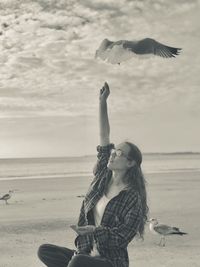 Woman feeding birds at beach against sky