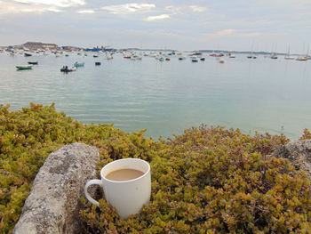 Coffee cup by sea against sky