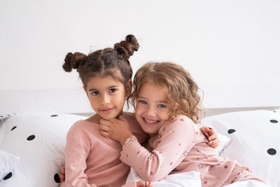 Portrait of smiling sisters sitting on bed at home