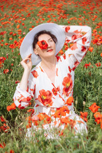 Close-up portrait of woman in summer dress among the field with blooming poppies against a sky