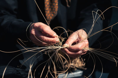 Unrecognizable senior person making wicker from natural material on sunny day