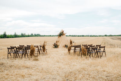 Wooden chairs on field against sky