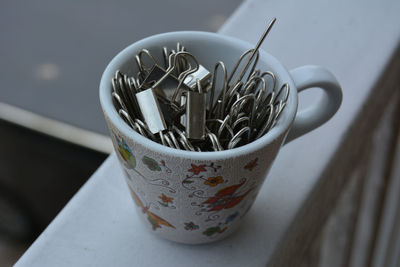 Portrait of a tiny cup filled with metal binder clips on a white surface 