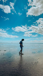 Rear view of woman standing at beach against sky