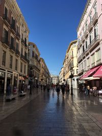 People walking on street in city against clear blue sky