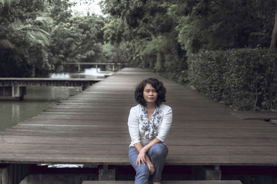 Portrait of woman sitting on railing against trees