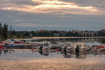 Boats moored in city against sky during sunset