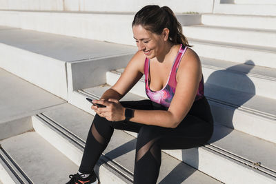 Smiling female athlete text messaging through smart phone while sitting on steps