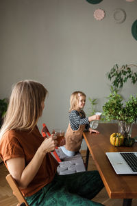 Mother with tea cup rests and looks at child who watering green plants