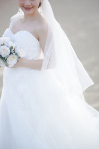 Midsection of bride holding bouquet while standing on road
