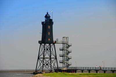 Lighthouse by sea against clear sky