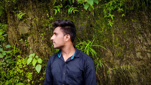 Young man looking away while standing against plants