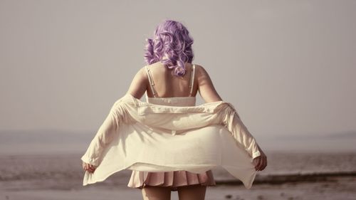 Rear view of woman standing at beach against sky