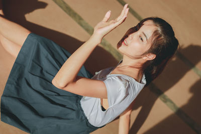 High angle view of young woman shielding eyes while sitting on floor