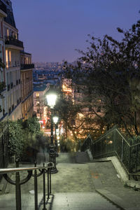 Illuminated street by buildings against sky at night