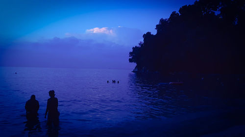 Silhouette man standing by sea against blue sky