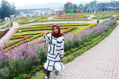 Portrait of smiling young woman standing by flowering plants