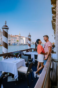 Couple embracing while standing at cafe by canal against sky