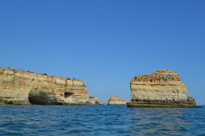 Rock formations in sea against clear blue sky