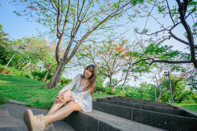 Portrait of smiling young woman sitting against trees