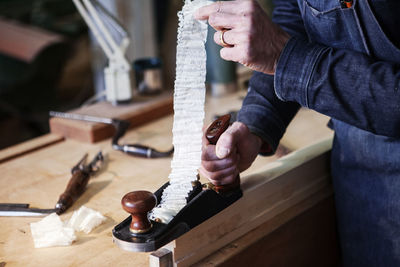 Midsection of carpenter planning wooden plank in workshop