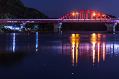 Illuminated bridge over river against sky at night