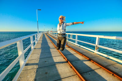 Full length of excited woman jumping on pier by sea against sky
