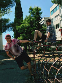 Rear view of people sitting on sidewalk against trees