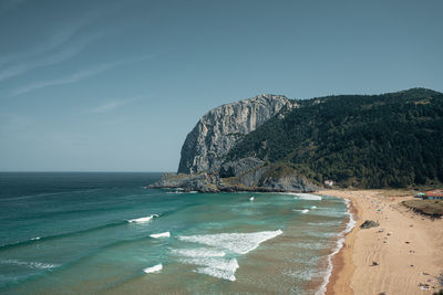 Scenic view of beach next to giant rock against sky