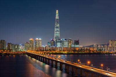 Lotte world tower in illuminated city by river at night