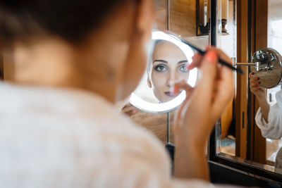 Portrait of young woman applying make-up with reflection on mirror
