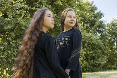 Two little girls, sisters with extra long curly shiny hair hold hands in park, nature on background