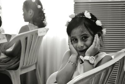 Portrait of happy girl wearing tiara sitting on chair at home