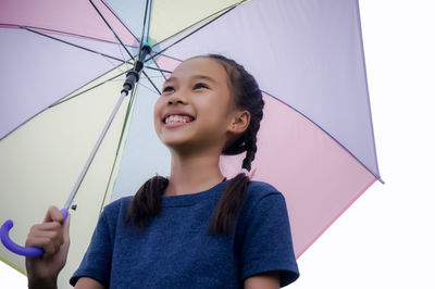 Low angle view of smiling girl holding umbrella standing against clear sky