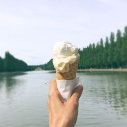 Close-up of hand holding ice cream against lake