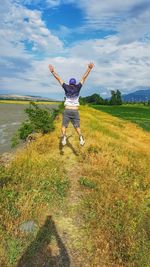 Rear view of boy jumping on field against sky