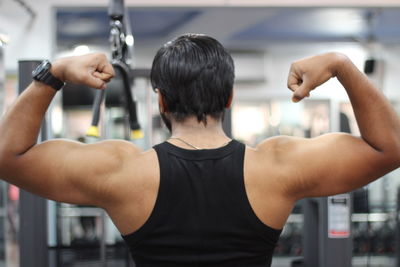 Rear view of man flexing muscles at gym