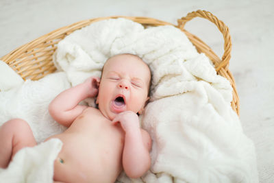 Cute baby boy yawning in basket at home