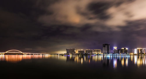 Illuminated buildings by river against sky at night