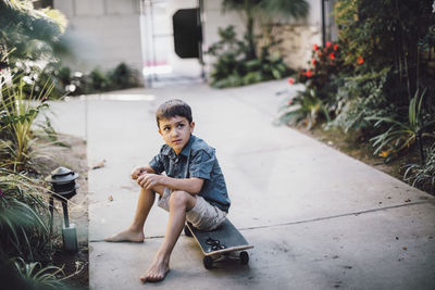 Boy looking away while sitting over skateboard on footpath