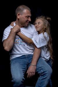 Full length of father and daughter against black background