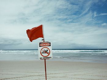 No swimming sign at beach against sky