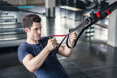 Athlete sporty man doing exercise with fitness trx straps to strengthen his abdominal muscle in gym.