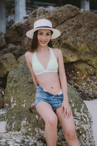 Portrait of smiling woman sitting on rock at beach