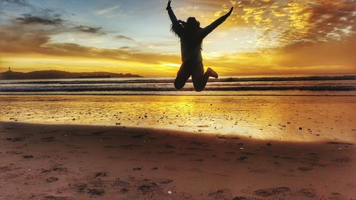 Silhouette man jumping on beach against sky during sunset