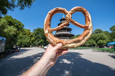 Close-up of hand holding pretzel against sky