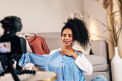 Smiling young woman showing dress while filming at home