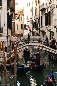 Gondolier rowing gondola on canal under arch bridge in city